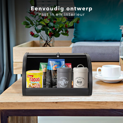 Mat zwarte Cheqo® broodtrommel met schuifdeksel en diverse items op een houten tafel in een moderne keuken.